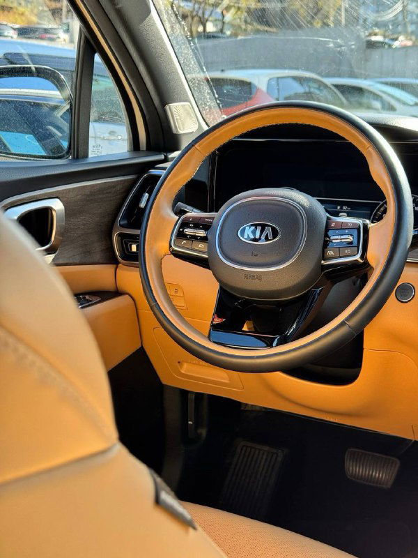 Крупный план рулевого колеса и панели KIA Sorento с коричнево-бежевой отделкой салона, акцент на логотипе KIA и элементы управления.