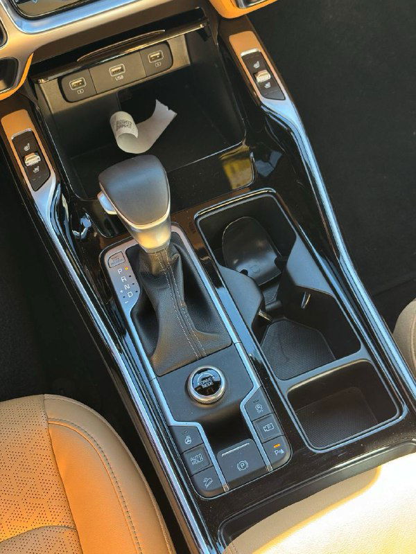 Крупный план селектора коробки передач, подстаканников и отделки центрального тоннеля KIA Sorento с глянцевыми и матовыми элементами.