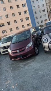 Общий вид автомобиля Honda Freed на стоянке со стороны — вертикальное кадрирование, авто между машинами, возможный кадр из видеообзора для объявления.