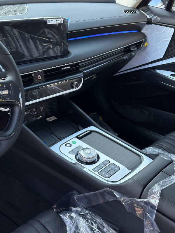 Центральная консоль KIA K8 Signature 2024: крупный план селектора, медиасистемы и отделки салона с защитной плёнкой, демонстрация новой эргономики.