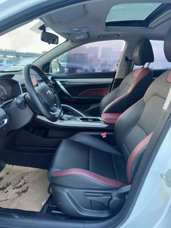 Передние сиденья Geely Coolray в чёрно-красной отделке, салон чистый, видна часть панорамной крыши и элементы управления на потолочной консоли.