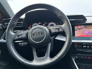 Крупный план руля Audi с логотипом, часть цифровой приборной панели и экран с камерой заднего вида, состояние элементов управления