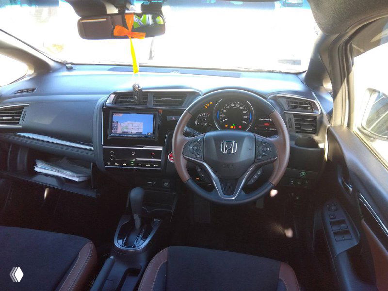 Салон Honda Fit 2018: общий вид приборной панели, мультимедиа-экран и рулевое колесо, состояние салона видно на фото, сиденья в коричневой отделке.