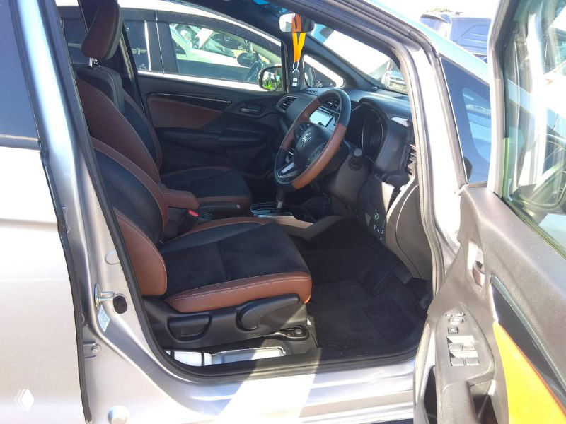 Вид на передние сиденья Honda Fit 2018 с открытой дверью: коричневая отделка сидений, место водителя, состояние обивки и торпедо.