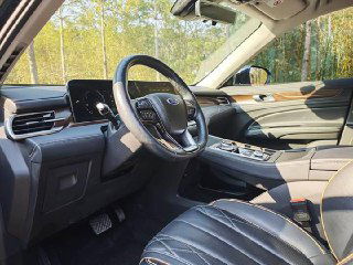 Водительская зона Ford Equator: руль, левый бок дверного проёма и элементы управления на руле в светлом салоне с коричневой отделкой.