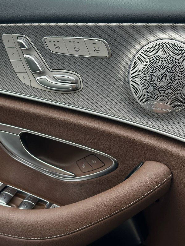 Дверная карта Mercedes E350: элементы управления положением сиденья, динамик Burmester и отделка из металла и коричневой кожи на внутренней панели двери.