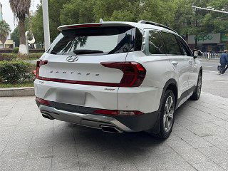 Задний вид белого Hyundai Santa Fe 2021 года — кормовая часть на парковке: багажник, светодиодные фонари, надпись SANTA FE и двойной выхлоп.