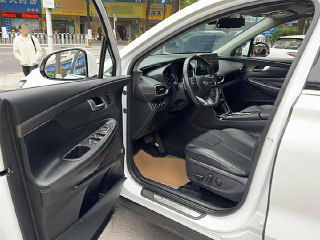 Открытая передняя дверь и водительское место Hyundai Santa Fe: крупный план панели, руль, рычаги, электрорегулировки сиденья и отделка салона.