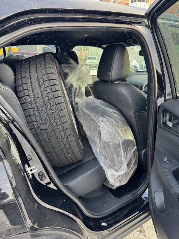 Задняя дверь открыта, в салоне лежит запасное зимнее колесо Mitsubishi Eclipse Cross и упакованные колёса — демонстрация комплектации и комплекта шин для клиента.