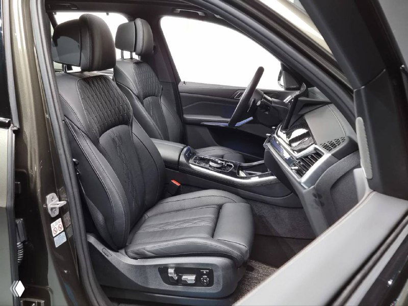 Фотография передних сидений BMW X5 с открытой дверью; видна регулировка кресел, обивка и интерьерная отделка в тёмных тонах.