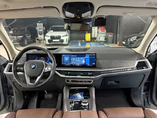 Фотография интерьера BMW X5 xDrive 50e xLine: панель приборов, большой экран мультимедиа и коричневая отделка сидений, видно пространство переднего ряда.