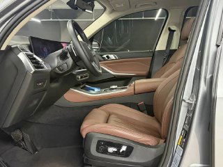 Снимок водительского места BMW X5 xDrive 50e xLine: руль, кнопки управления, боковой профиль кресла и отделка дверной панели коричневого цвета.