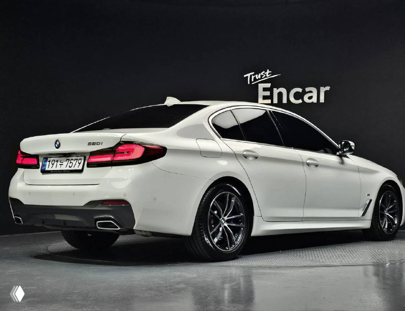 Трёхчетвертной вид сзади белого BMW 520i M Sport 2023 года: видны задние фонари, линия крыши и выхлопная система на студийном фоне.