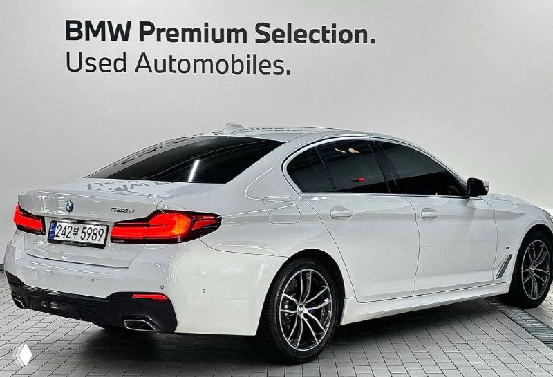 Белый BMW 523d M Sport — вид сзади и лёгким ракурсом, видно бампер, фонари и надпись об официальной программе подержанных автомобилей.
