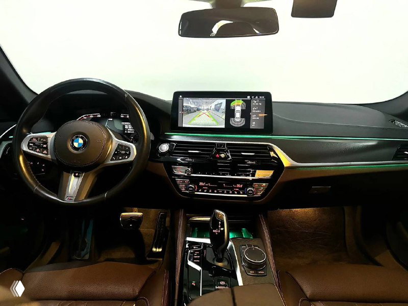 Интерьер BMW 523d M Sport: вид на руль, приборную панель и центральный экран с картой навигации, акцент на отделку и подсветку.