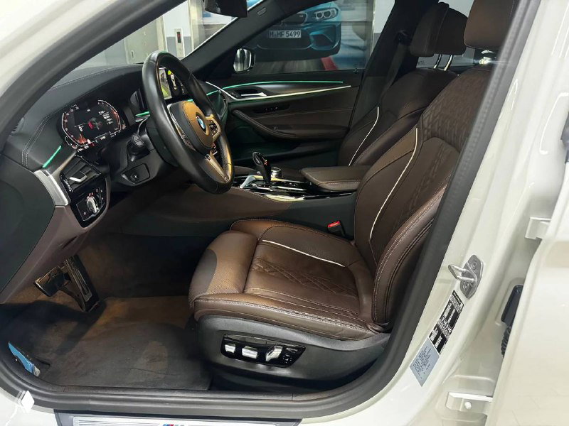 Переднее сиденье BMW 523d M Sport: коричневая кожаная обивка, электрорегулировки и декор дверной панели на светлом фоне.