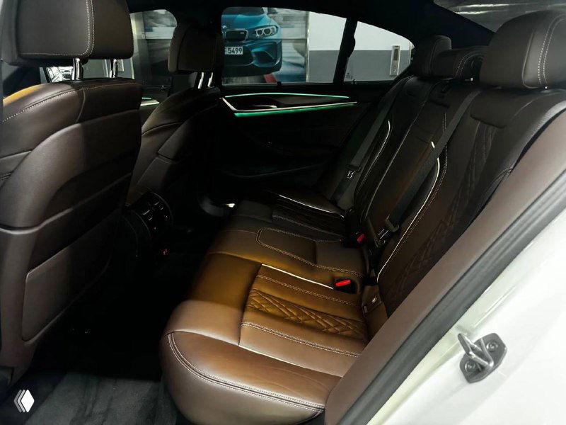 Задний ряд сидений BMW 523d M Sport: коричневая кожаная обивка, пространство для ног и центральный подлокотник, вид со стороны дверного проёма.