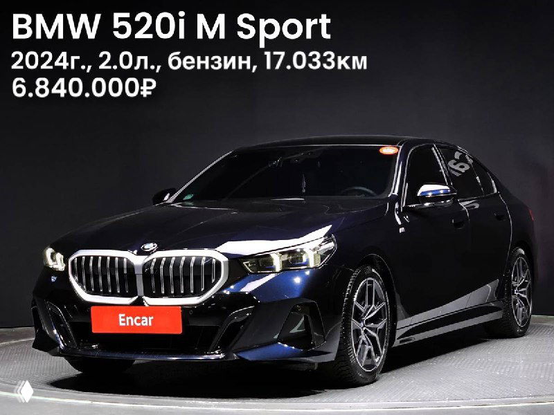 Фотография тёмного BMW 520i M Sport 2024 года — вид спереди в выставочном зале, указаны год, объём двигателя, пробег и цена на изображении.