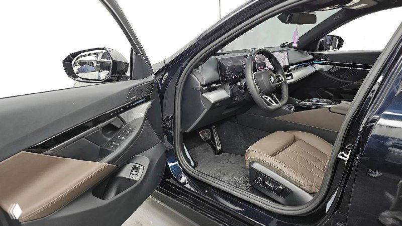 Ракурс открытой водительской двери тёмного BMW 520i M Sport — сиденье водителя, панель управления и боковой проём двери видны в кадре.