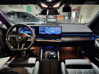 Снимок салона BMW 523d M Sport — крупный план приборной панели, мультимедиа и рулевого колеса, видна ночная подсветка интерьера.