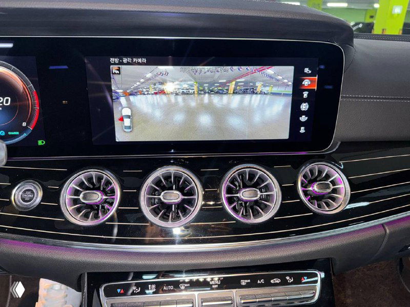 Центральная консоль Mercedes‑Benz CLS450 с включённым экраном мультимедиа, изображение камеры заднего вида и элементы управления кондиционированием и мультимедиа.