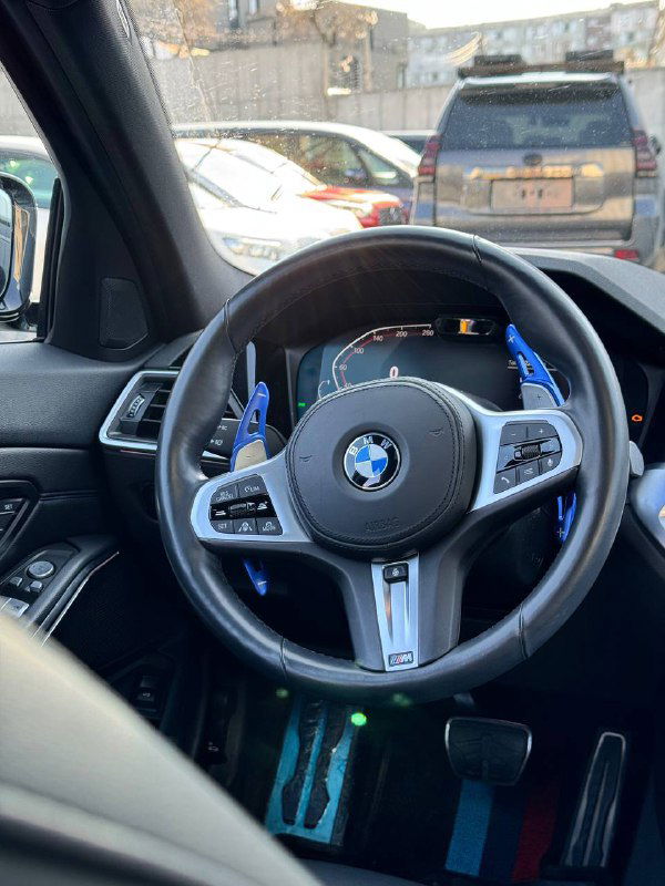 Вид руля и приборной панели BMW 320i 2021 M‑Sport — мультифункциональный руль, подсветка элементов, общий вид центральной части салона с водительской позиции.
