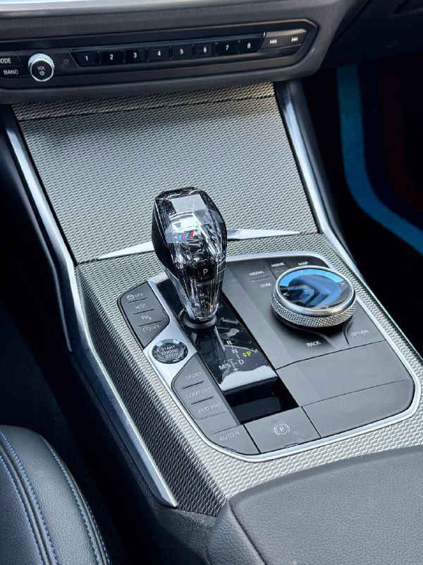 Селектор коробки передач и функциональные элементы управления на центральной консоли BMW 320i 2021 M‑Sport — кристаллический рычаг селектора и регулятор iDrive.