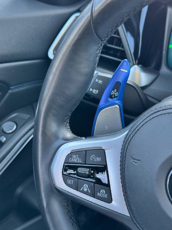 Крупный план руля с лепестками переключения и кнопками управления — на фото видны синие декоративные элементы M‑Sport и клавиши круиз‑контроля.