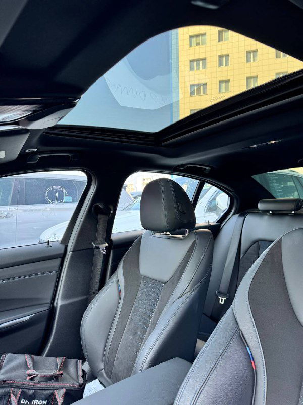Вид на панорамную крышу и передние сиденья BMW 320i 2021 M‑Sport — интерьер, отделка сидений, обзор пространства над головой с увеличенным световым проёмом.