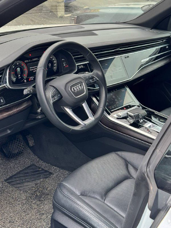 Вид салона Audi Q8 со стороны переднего пассажира: рулевая колонка, переднее кресло и отделка дверей.