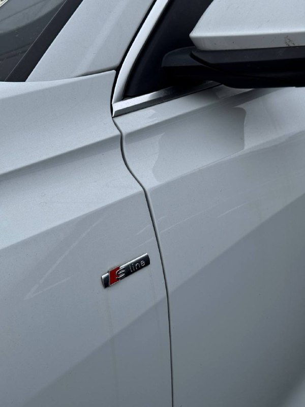 Боковой фрагмент корпуса Audi Q8 с эмблемой S-Line на крыле, светло‑серый лак и ровные зазоры между панелями.