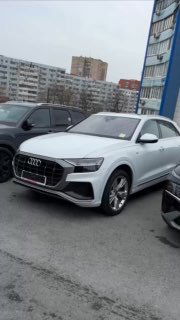 Общий вид Audi Q8 в стоянке с другой перспективы: модель, цвет и интерьерные наклейки заметны через стекло.