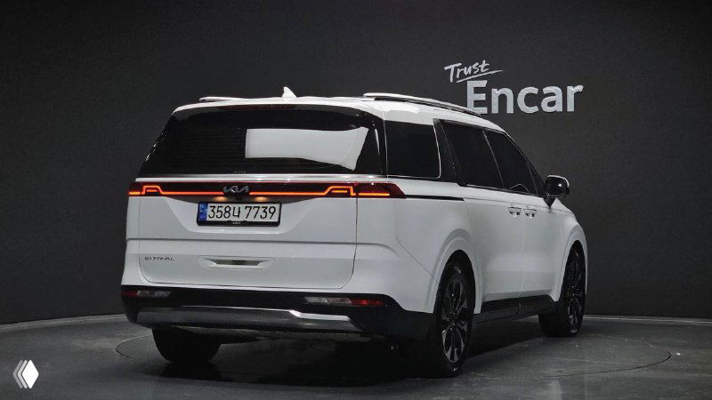 KIA Carnival Signature 2021 — вид сзади и сбоку на студийном фоне; заметна светлая окраска, фонари, эмблема и общие пропорции минивэна.