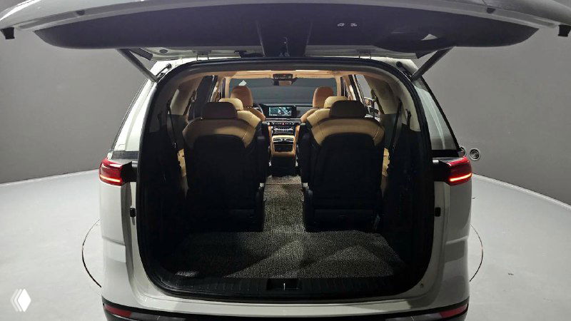 Открытый багажный отсек KIA Carnival Signature 2021 — вид из задней части салона на пространство для груза и складывающиеся сиденья, подсветка салона.