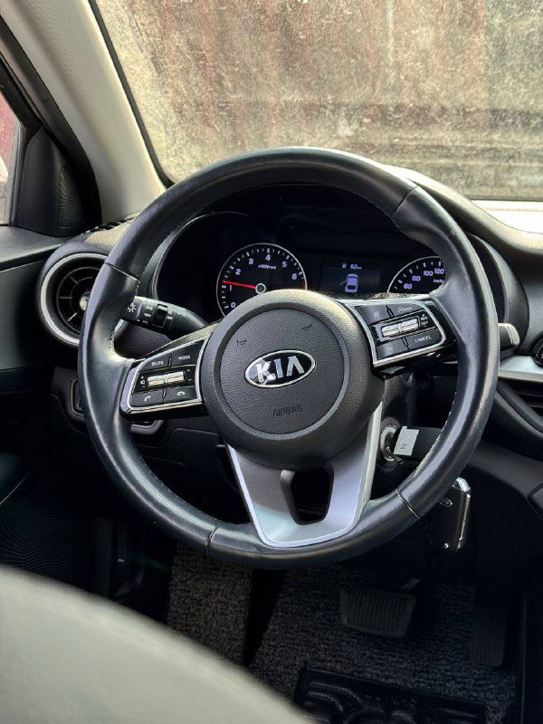 Крупный план рулевого колеса KIA K3 с логотипом на центре и многофункциональными кнопками; видна текстура обивки и часть приборной панели рядом.