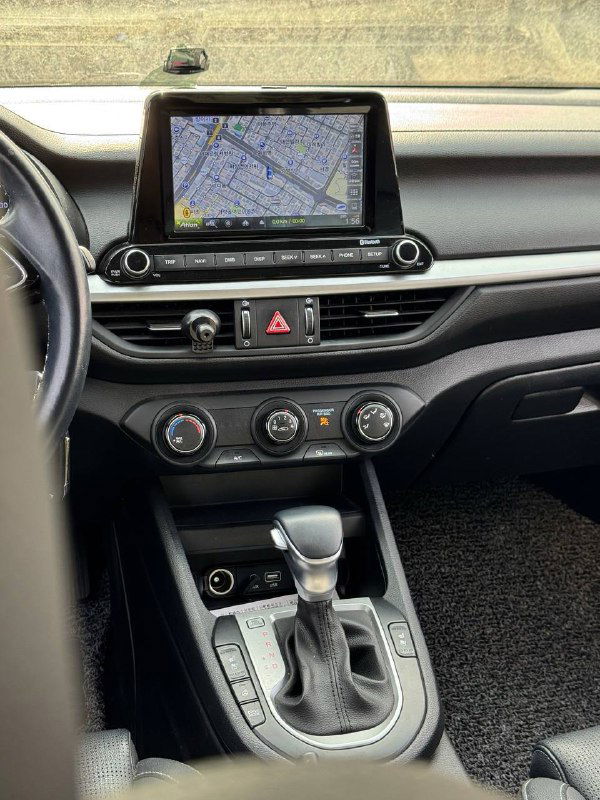 Центральная панель KIA K3 с включённым сенсорным экраном навигации, карта на дисплее, элементы управления климатом и декоративные вставки перед водителем.