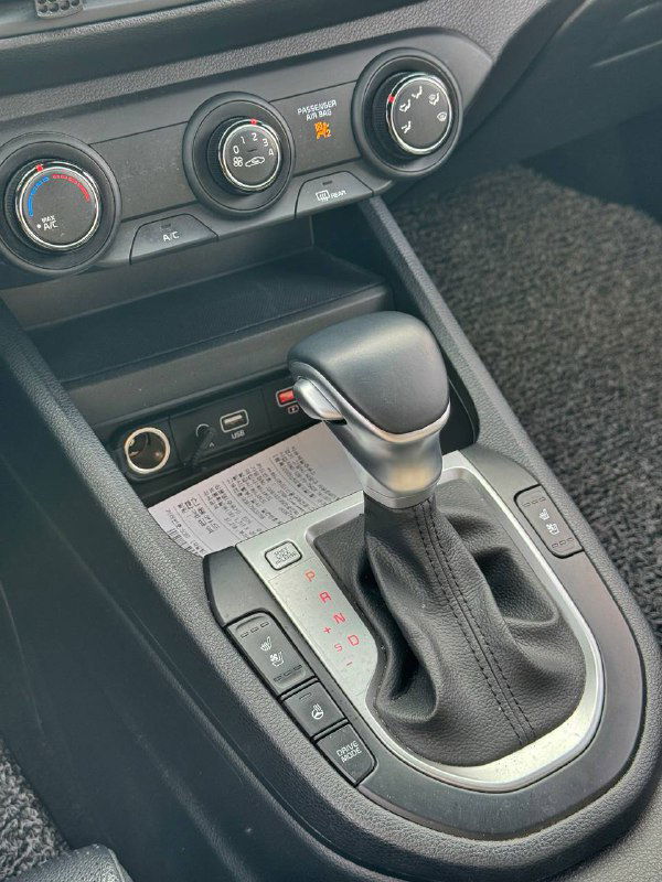Селектор автоматической коробки передач KIA K3 вблизи; видны подстаканники, разъёмы питания и элементы управления режимами трансмиссии на центральной консоли.