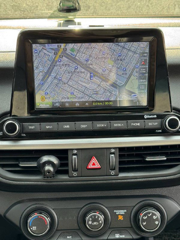 Крупный план экрана мультимедиа KIA K3 с отображением карты и дорог; панель вентиляции и кнопки аварийной сигнализации под экраном, видна приборная доска.