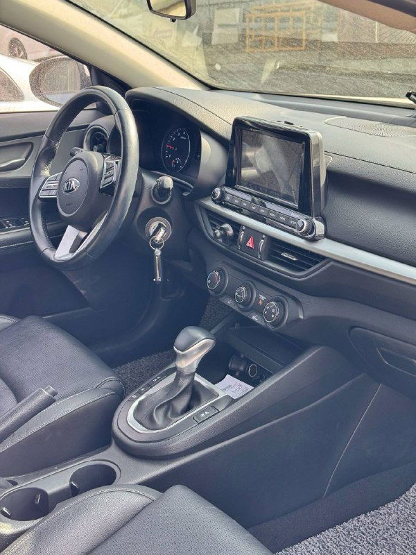 Угол обзора салона KIA K3 со стороны водителя: видны переднее сиденье, руль, панель приборов и центральная консоль в целом, обивка и отделка сидений.