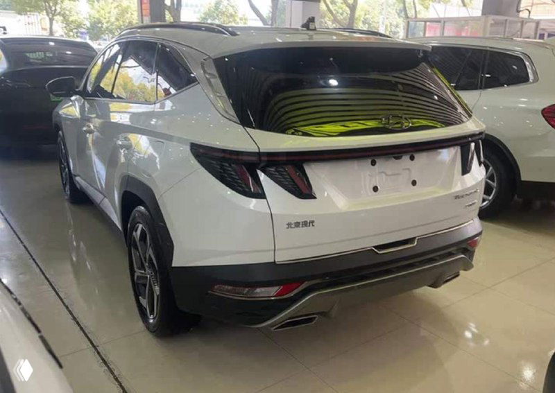 Задняя часть белого Tucson в шоуруме: открытая поверхность багажника, фонари и нижняя часть бампера, общий вид модели с китайского рынка без регистрационных знаков.