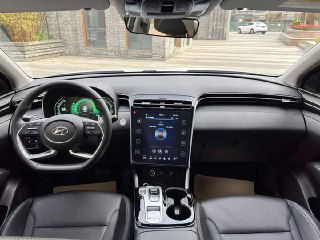 Салон Hyundai Tucson 2022: торпедо и водительское место в профиль, видна мультимедийная панель, руль и приборная панель автомобиля.