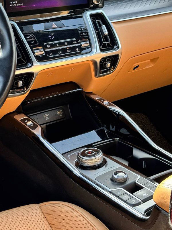 Центральная консоль KIA Sorento: мультимедийный экран, дефлекторы и элементы управления; контраст чёрных панелей и оранжевой отделки салона.