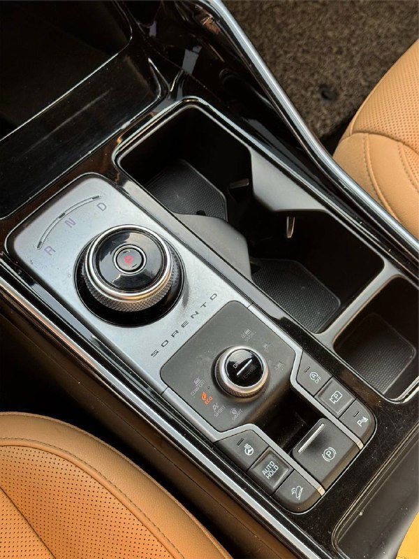 Блок управления коробкой передач с роторной шайбой, селектором и рядом кнопок; глянцевая чёрная отделка и подстаканники в салоне.