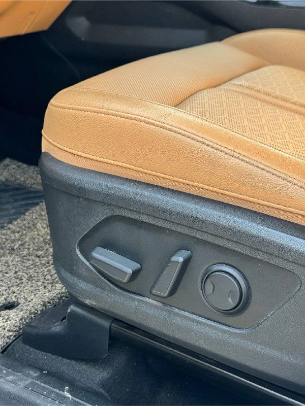 Крупный план боковой панели переднего сиденья с электроприводами регулировки и текстурой коричнево‑оранжевой обивки кресла KIA Sorento.