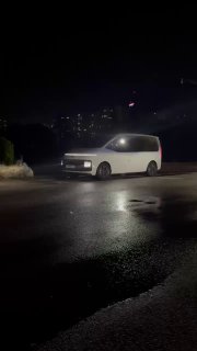 Ночной снимок белого минивэна Hyundai Staria на дороге в порту/окрестностях Пусана после погрузки, отражение на влажном асфальте