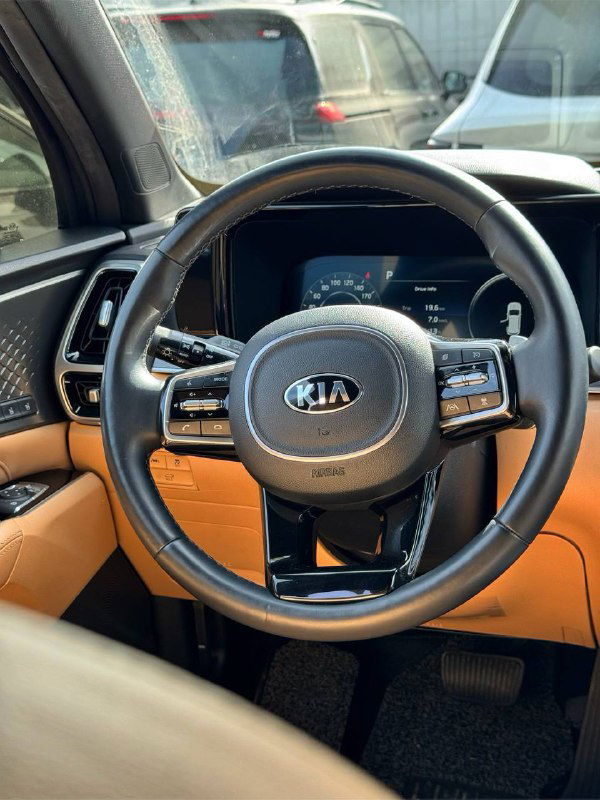 Крупный план рулевого колеса KIA Sorento: кожаный руль с логотипом Kia и кнопками управления, интерьер в бежевых тонах, вид с водительского места.