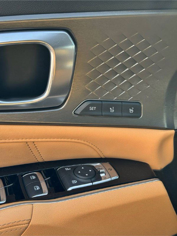 Детали дверной панели KIA Sorento: элементы управления стеклоподъемниками, память положений сиденья и декоративная отделка в бежевой и темной гамме.