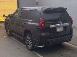 Задняя часть черного Toyota Land Cruiser Prado 2021 на автомобильной площадке, виден багажник и фон терминала для отправки в порт.