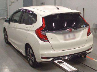 Белый Honda FIT 2017, вид сзади на площадке осмотра; видна задняя дверь и фон терминала отправки автомобилей.