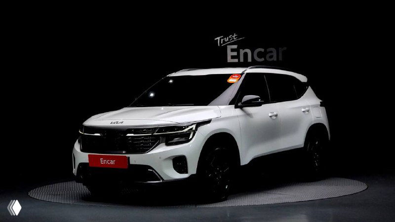 KIA Seltos 2022 светлого цвета на фоне затемнённой студии — общий вид автомобиля под другим углом, подчёркивающий форму и внешний дизайн.